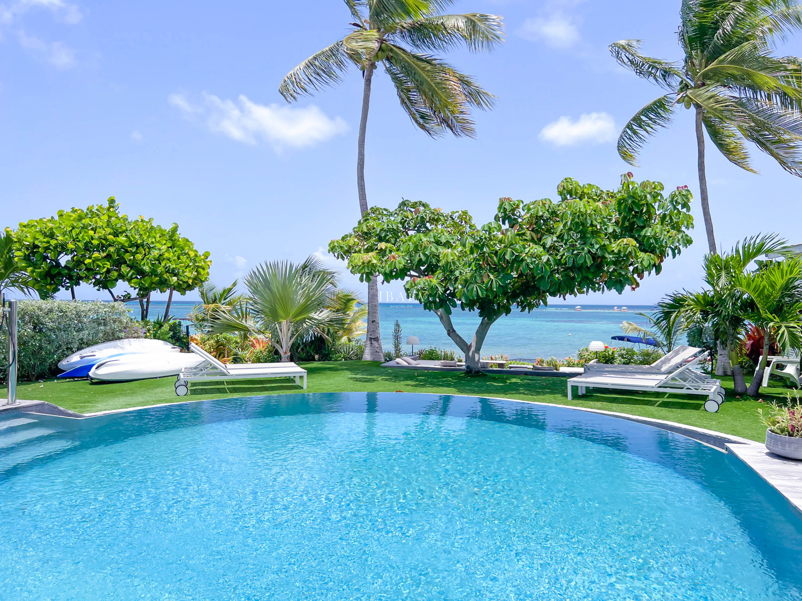 Ocean view of the infinity pool with coconut trees, sun loungers, and kayak on the lagoon of Saint-François