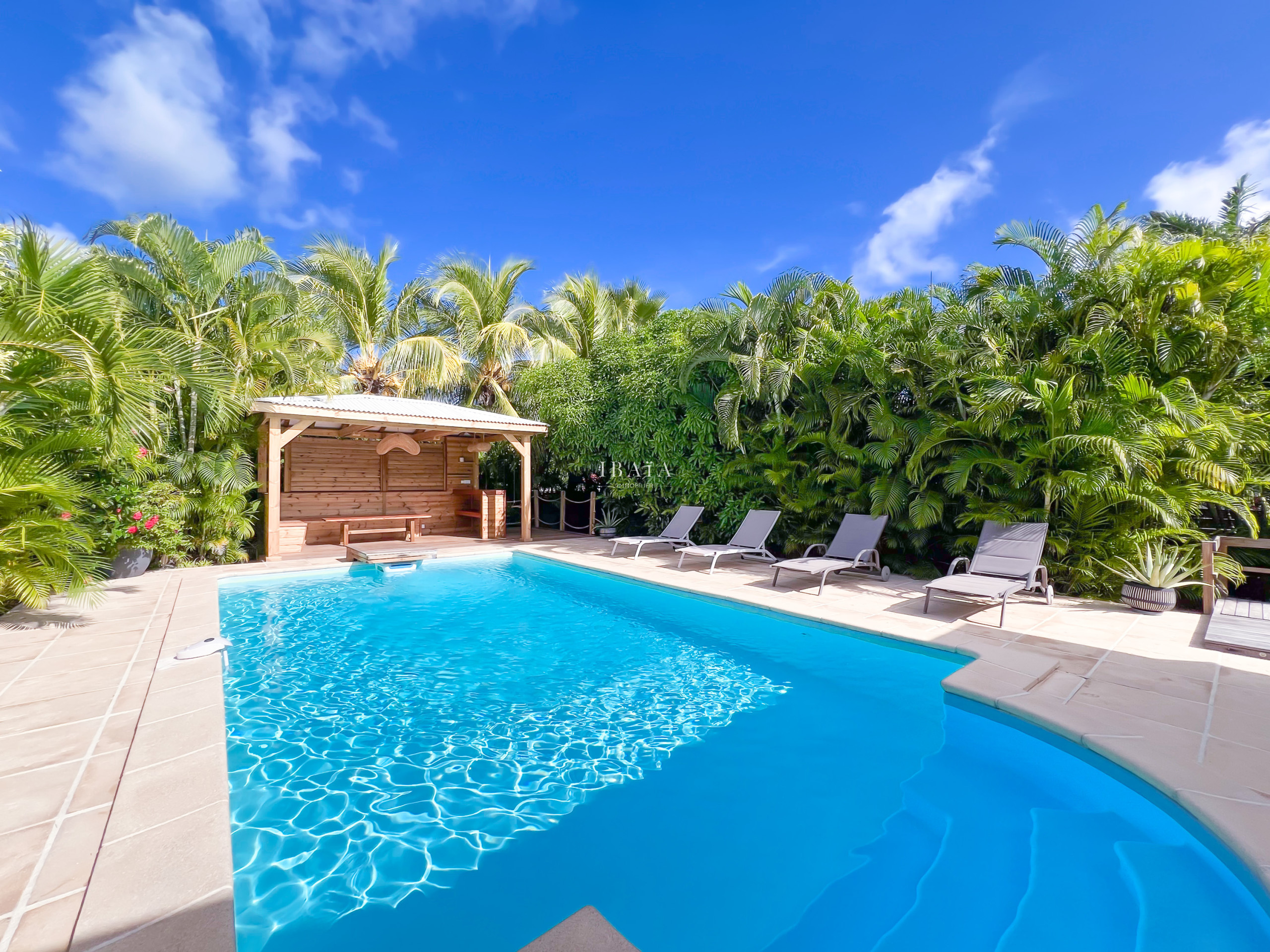 Freeform pool with wooden gazebo and sun loungers in tropical garden