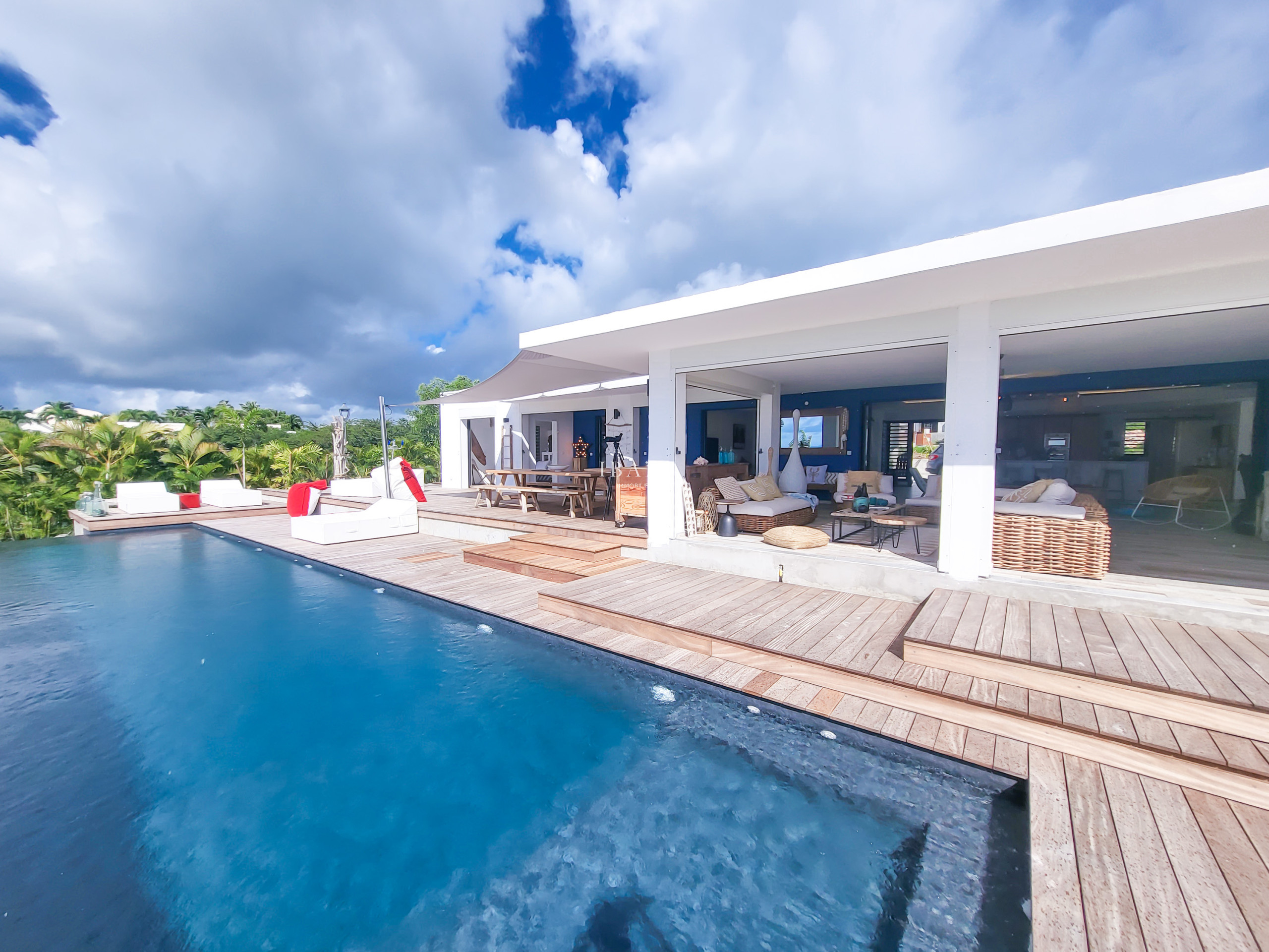 Modern white villa with infinity pool and wooden deck surrounded by tropical vegetation