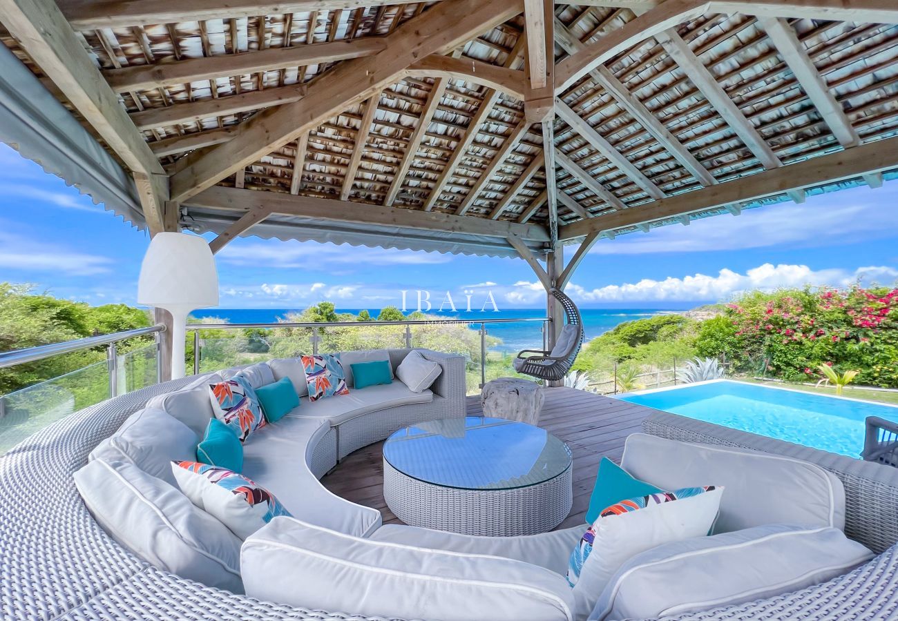 View of an 8-seater round garden lounge by the pool under a wooden patio, offering a view of the sea in our top-of-the-range villa in the West Indies