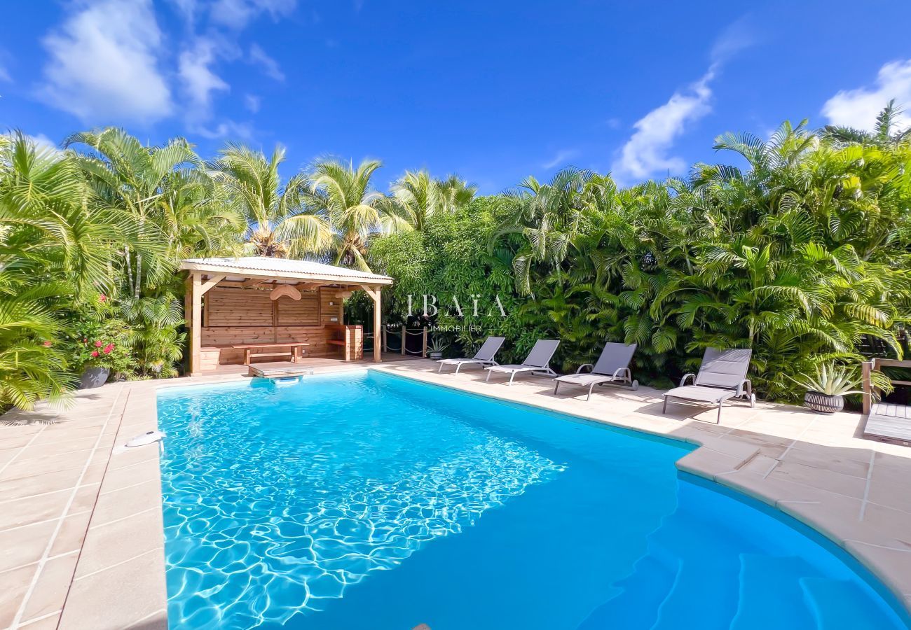 Freeform pool with wooden gazebo and sun loungers in tropical garden