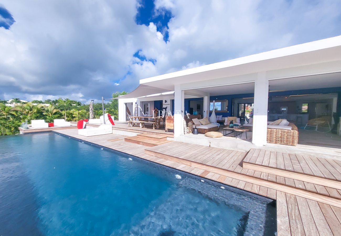 Modern white villa with infinity pool and wooden deck surrounded by tropical vegetation