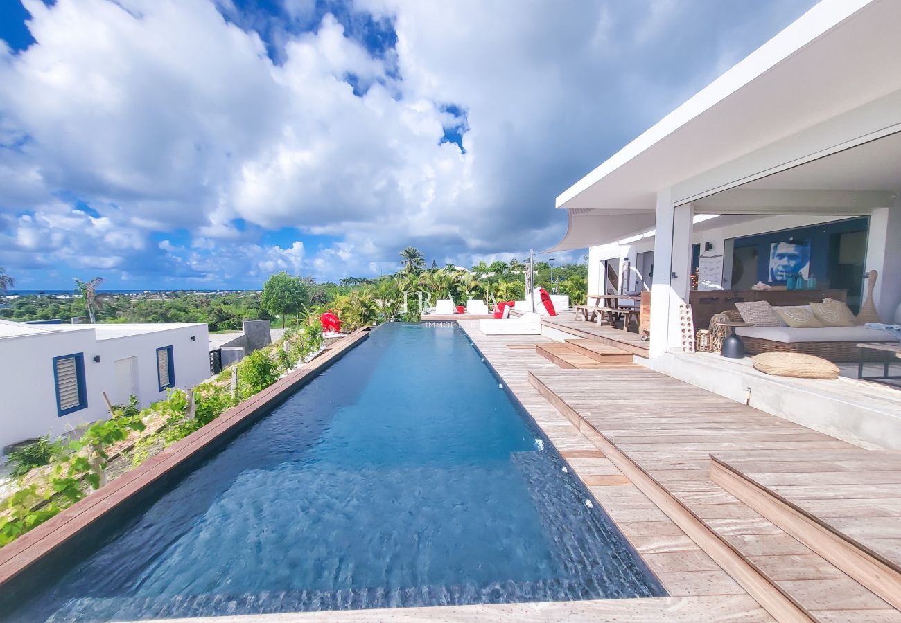 Long infinity pool with wooden deck and panoramic view over tropical landscape