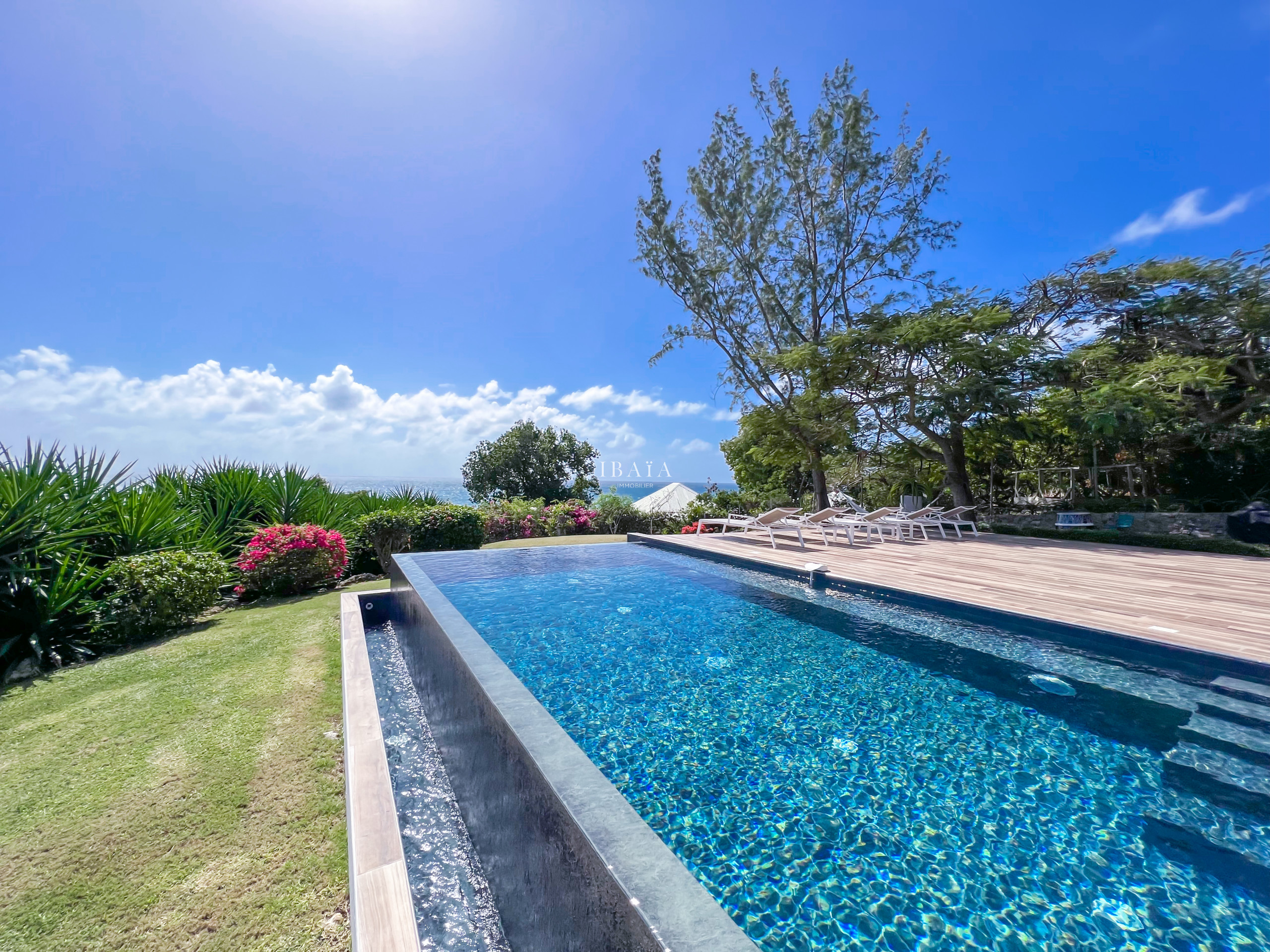 Piscina desbordante con vista al mar y jardín tropical florecido