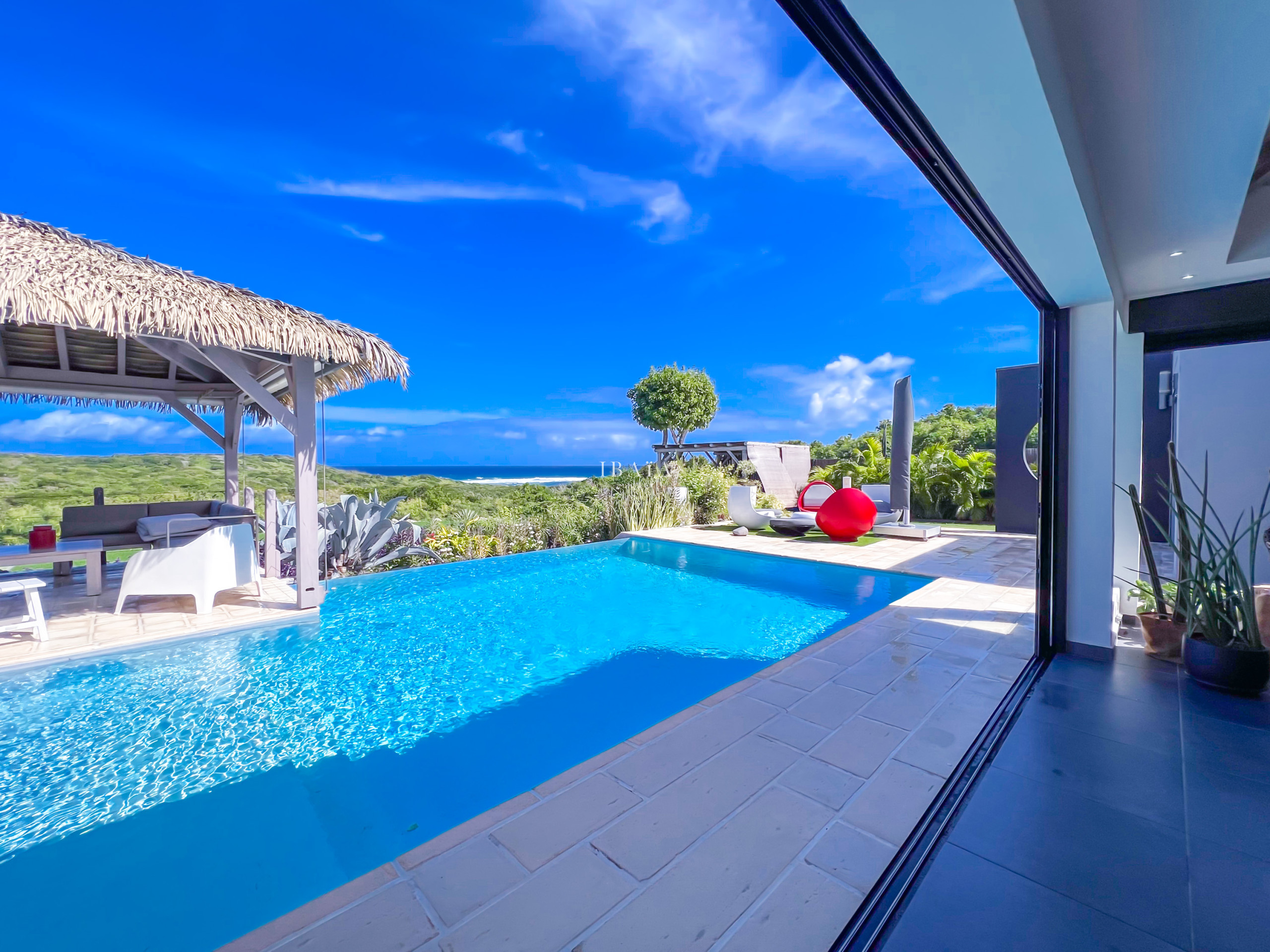 Piscina infinita con vista al mar y un gazebo de paja