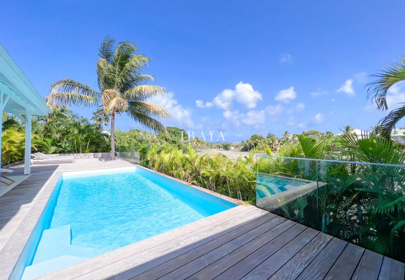 Vista de la piscina y el campo de golf de Saint-François desde la villa de lujo, rodeada de una terraza de madera y cocoteros en las Antillas.