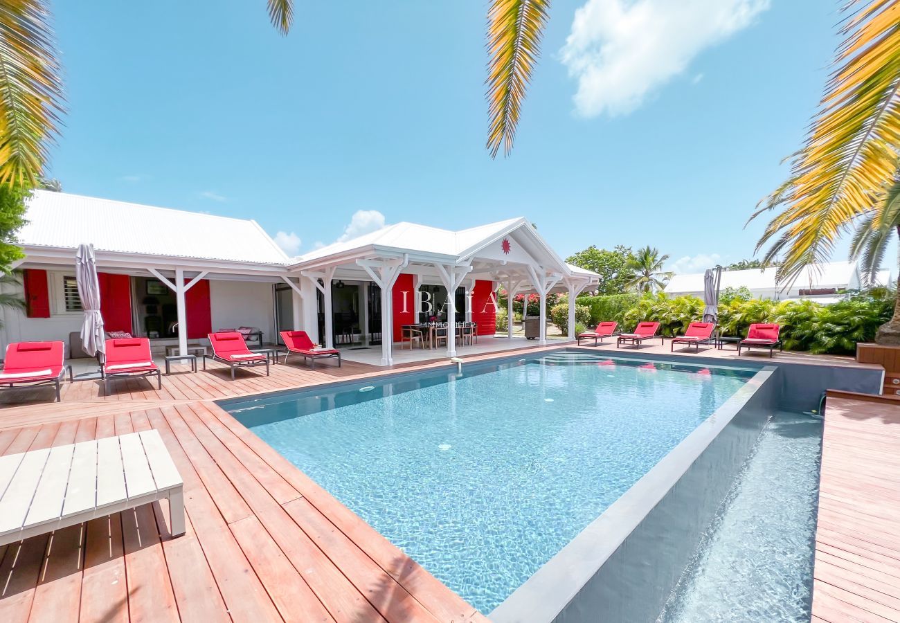 Vista de la piscina infinita rodeada de tumbonas rojas y la elegante fachada de la villa de alta gama en las Antillas.