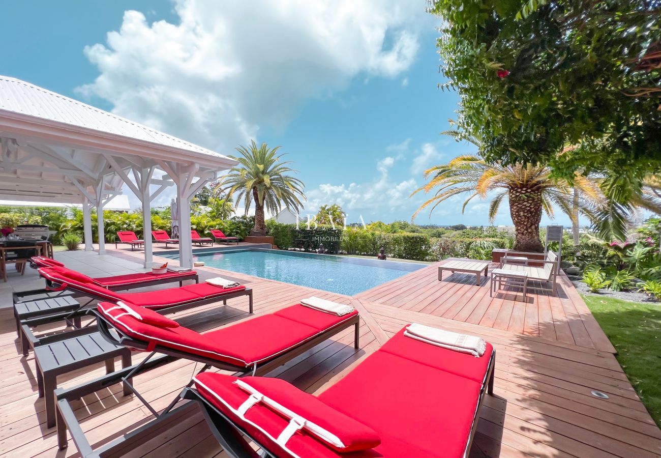 Vista de la piscina, las tumbonas rojas y el sillón de jardín alrededor de la piscina infinita con jardín tropical en una villa de alta gama en las An