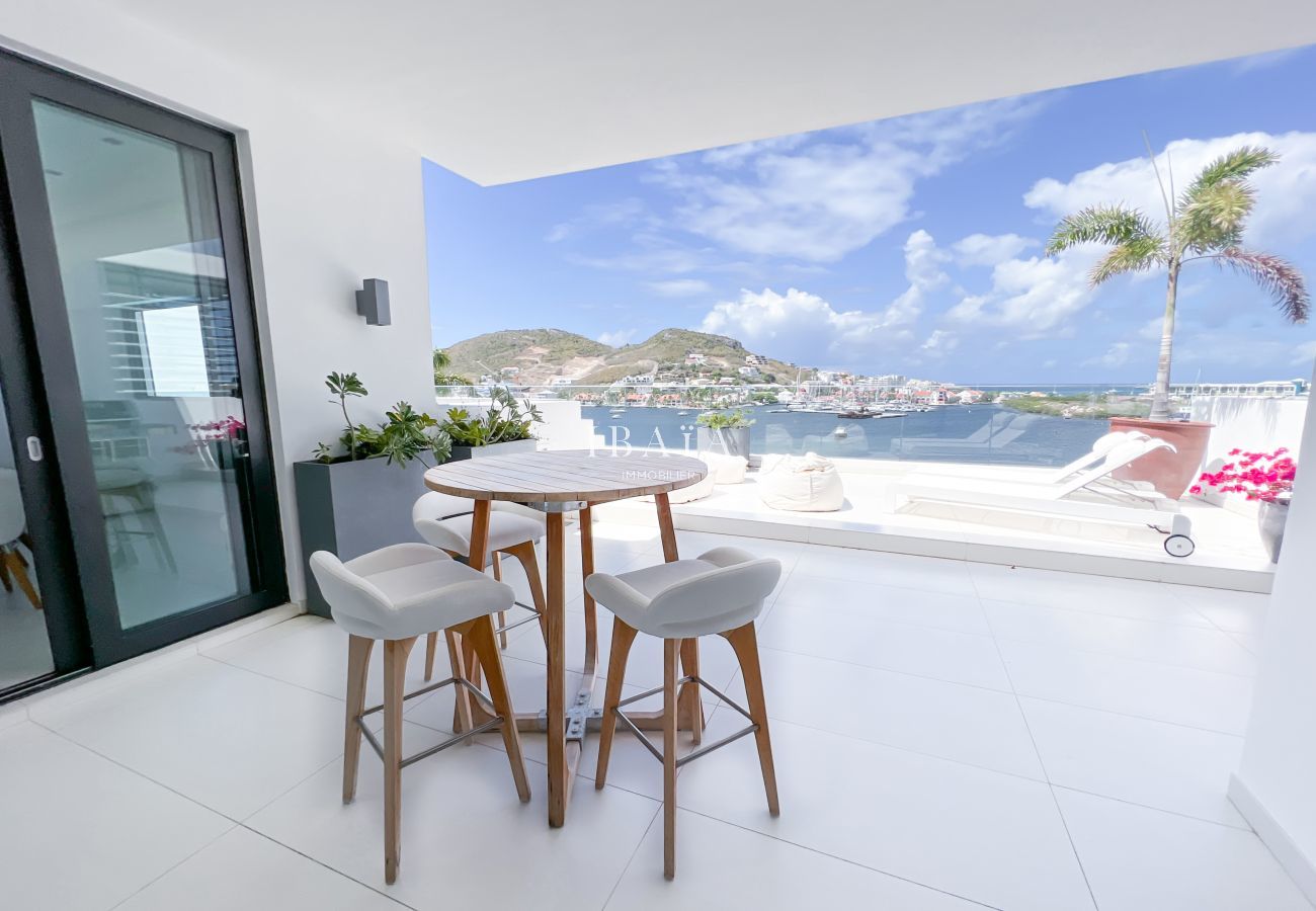 Vista de la terraza del ático con mesa exterior y silla alta, que ofrece vistas panorámicas ininterrumpidas sobre la bahía, en una villa de lujo en la