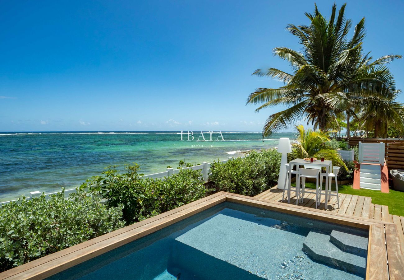 Vista de la piscina y el mar desde la terraza junto a la piscina, con una mesa alta de 4 plazas en nuestra villa de alta gama en las Antillas.