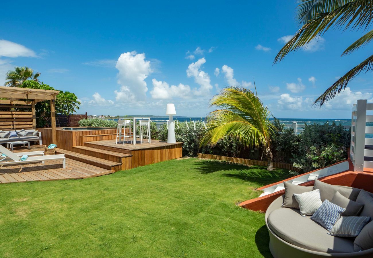 Vista del jardín con 2 tumbonas en la terraza de madera y una gran cama exterior desde nuestra lujosa villa junto al mar en las Antillas.