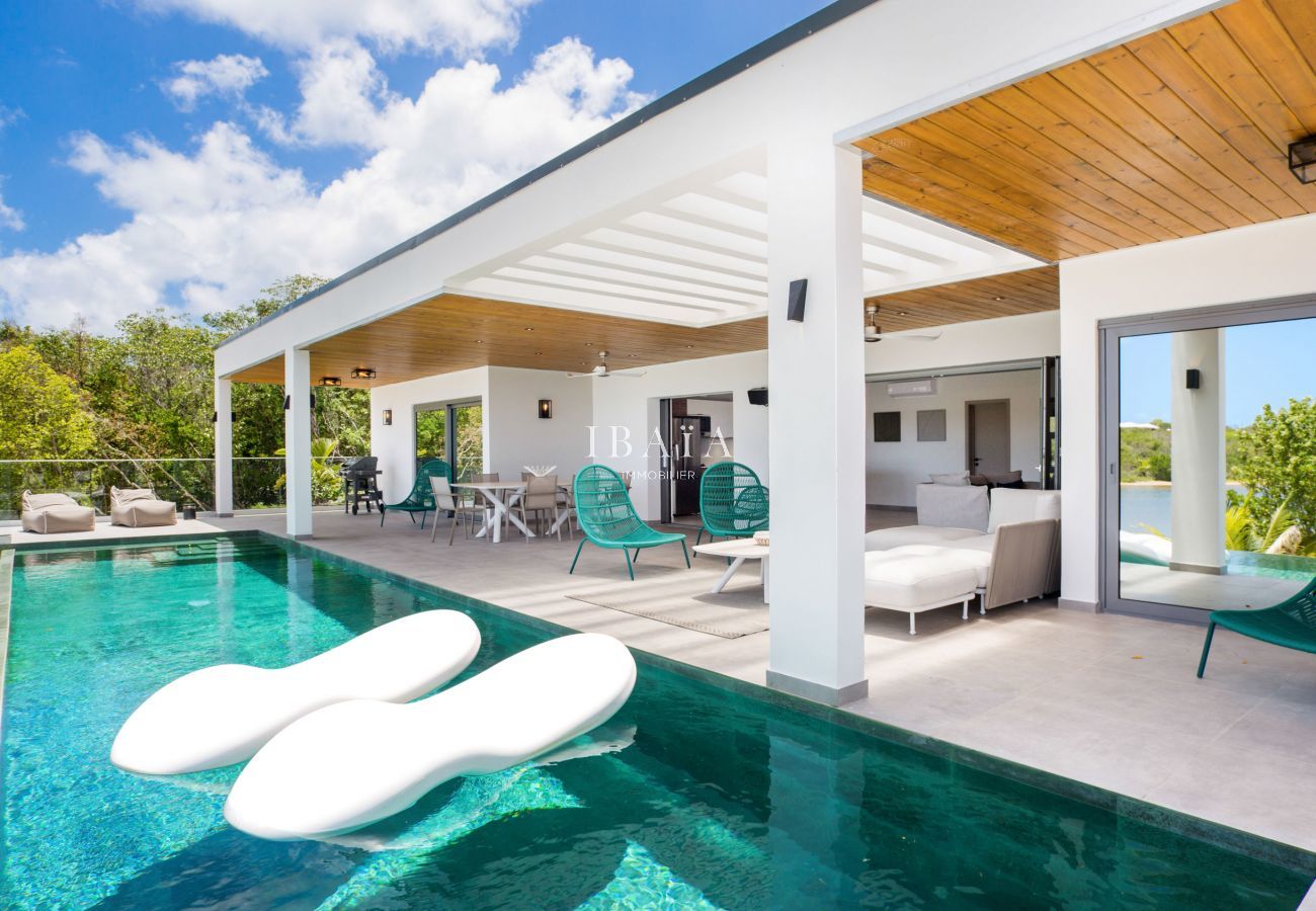 Vista de la piscina, terraza y pérgola con encofrado de madera, con 2 tumbonas flotantes en la piscina de nuestra villa de alta gama en las Antillas