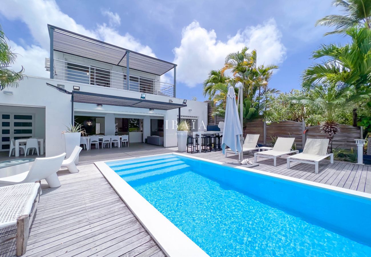 Piscina de la villa, terraza de madera, casa de dos niveles, tumbonas, sombrillas y vegetación tropical