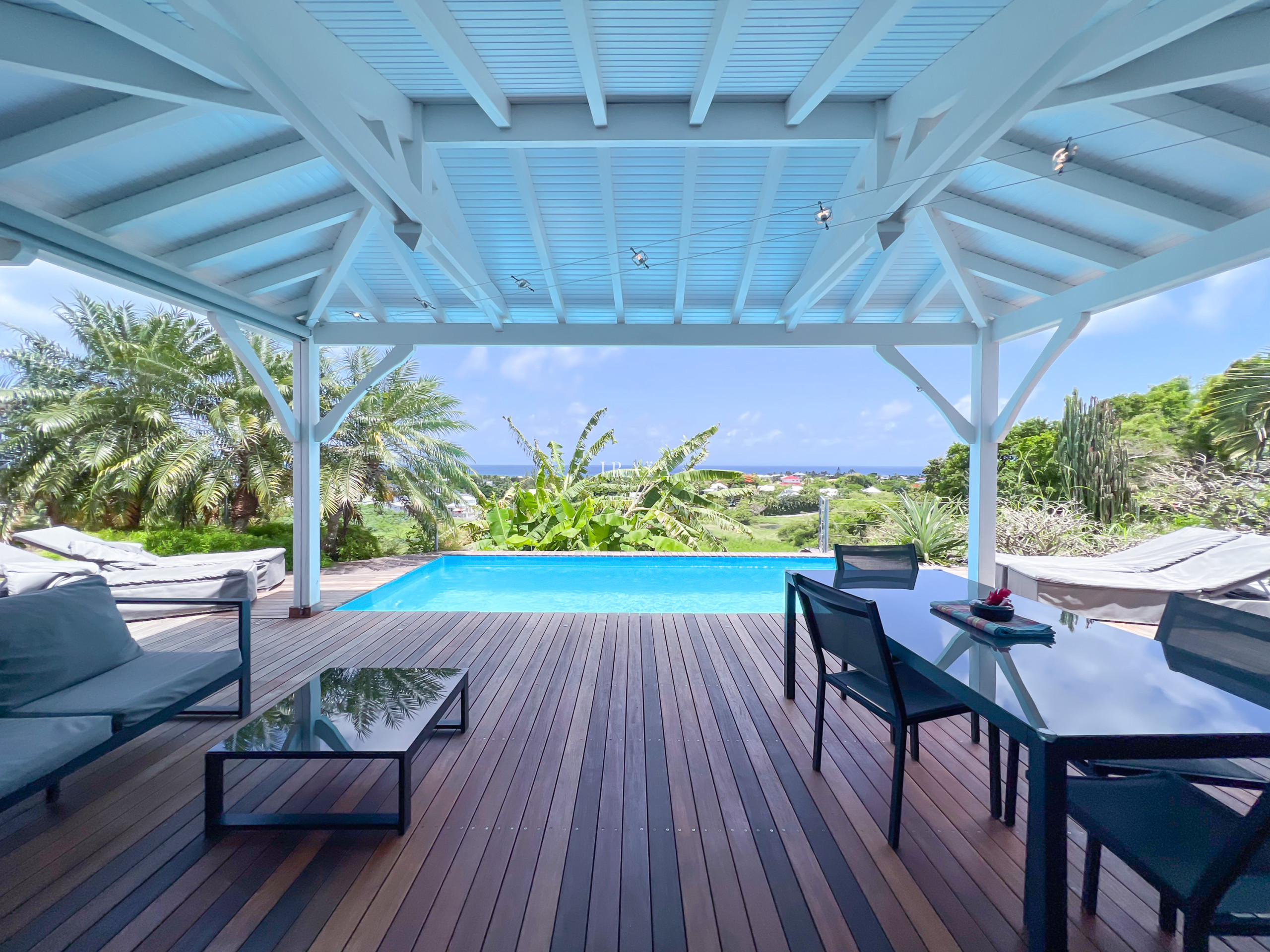 Vue d’une terrasse en bois avec piscine et végétation luxuriante