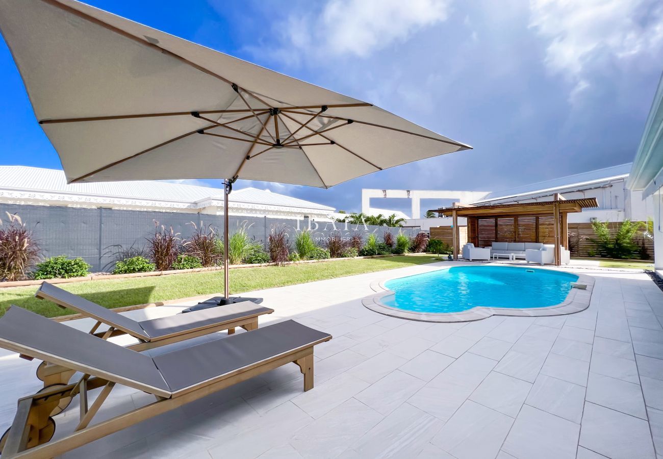 Vue sur la piscine, un transat, un parasol et un salon de jardin ombragé dans une villa haut de gamme aux Antilles, pour des moments de détente en ple