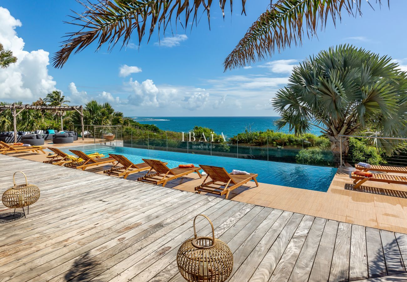 Vue de la terrasse en bois avec transats en bois, offrant une vue sur la piscine et l'océan, dans une villa haut de gamme aux Antilles