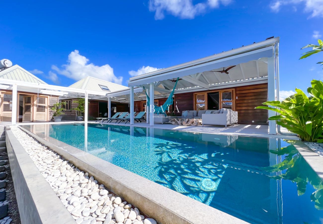 Piscine miroir devant la terrasse équipée de transats et d'un salon de jardin