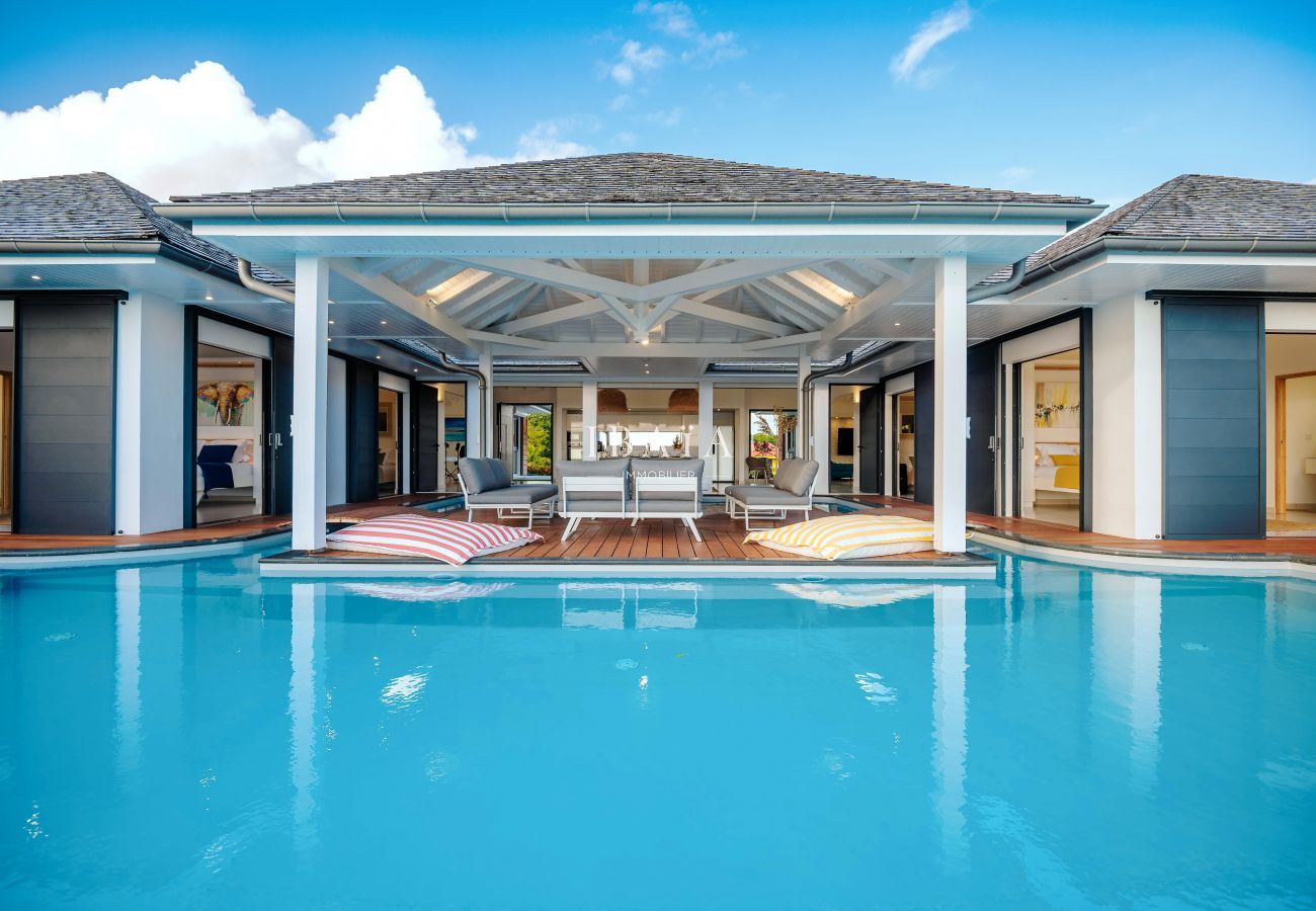 Maison de luxe avec piscine turquoise, terrasse en bois et intérieurs visibles.
